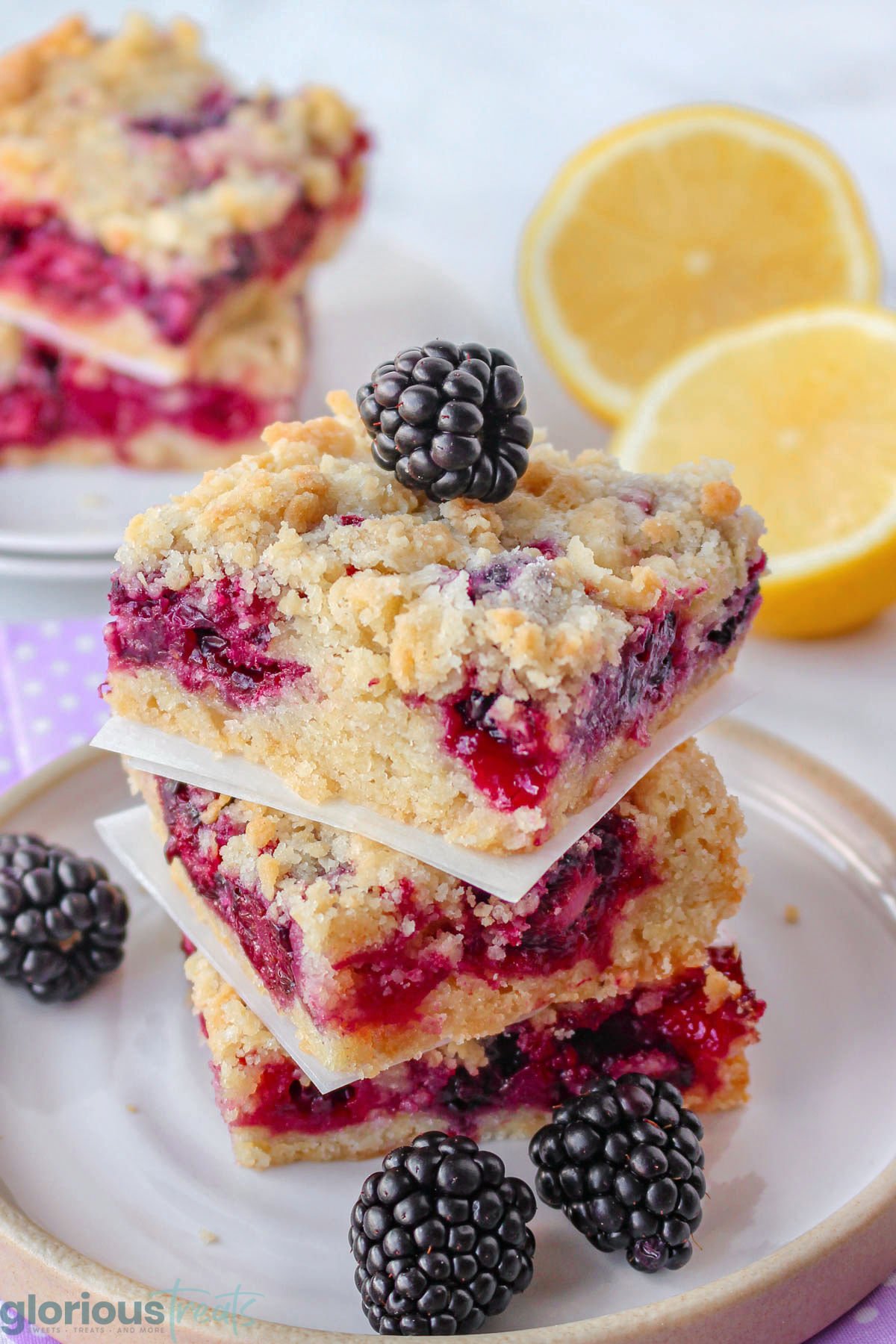 Stack of blackberry bars with crumb topping on white plate topped with a fresh blackberry.