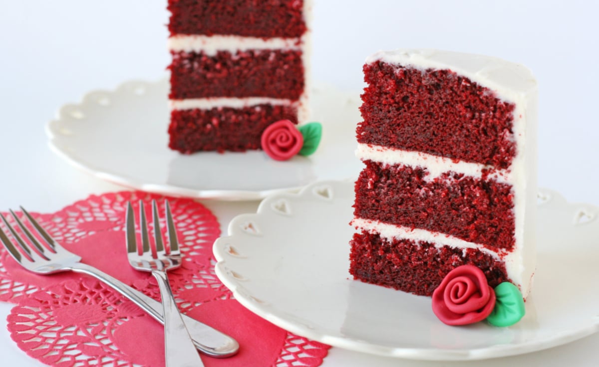 two slices of red velvet cake with fondant rose on white plate