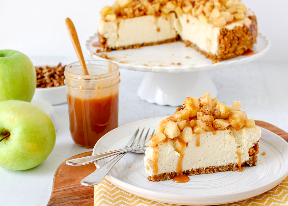 wide shot of a piece of cheesecake sitting on a white plate with the rest of the cheesecake in the background