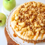 top down view caramel apple cheesecake recipe on white cake plate sitting on wood board