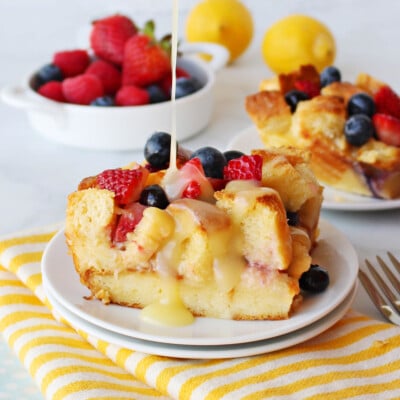 bread pudding made with fresh berries and drizzled with a lemon sauce sitting on white plate on a yellow and white striped towel.