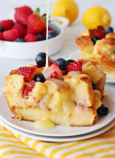 bread pudding made with fresh berries and drizzled with a lemon sauce sitting on white plate on a yellow and white striped towel.