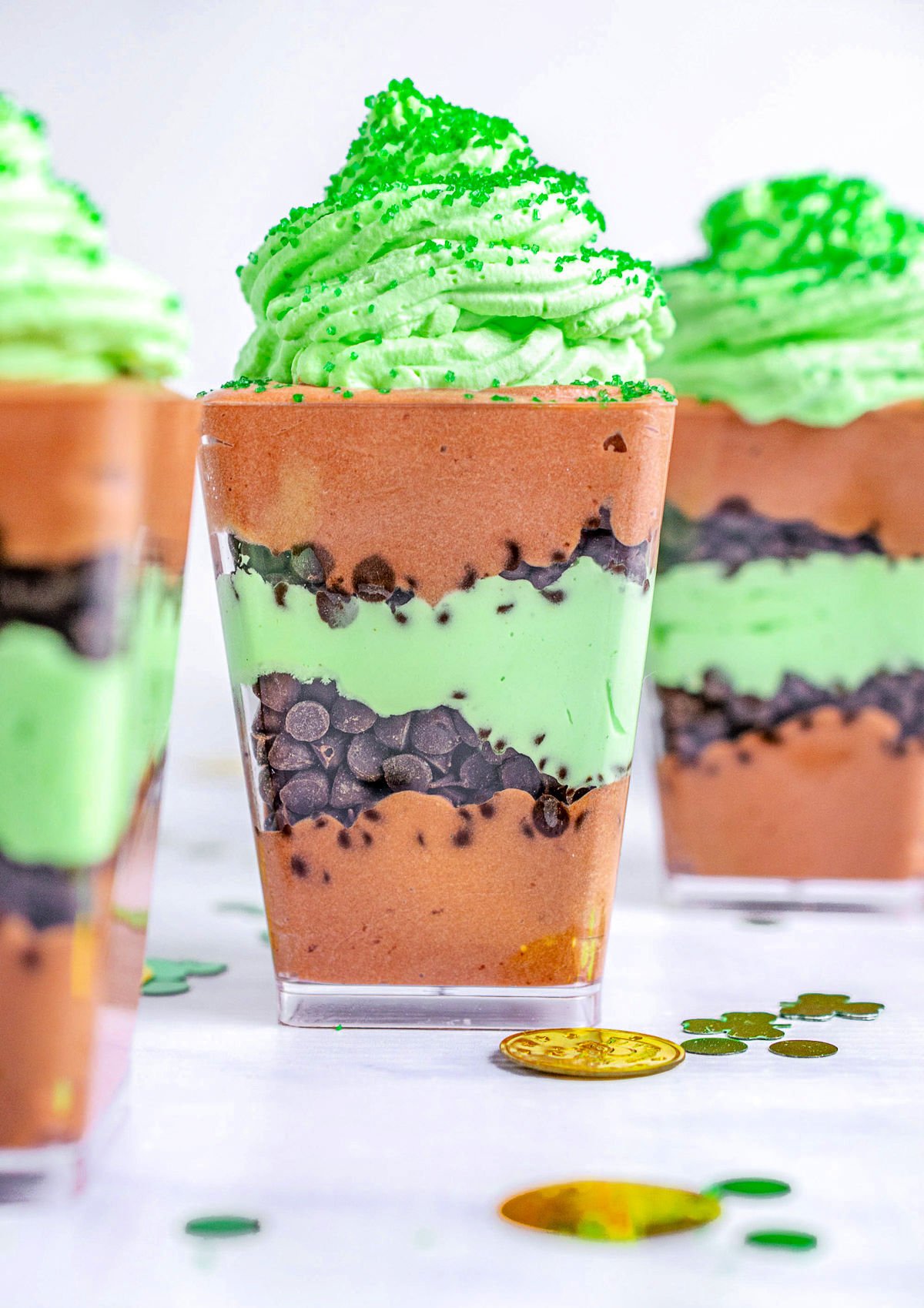 three dessert cups layered with chocolate pudding mint whipped cream and mini chocolate chips.