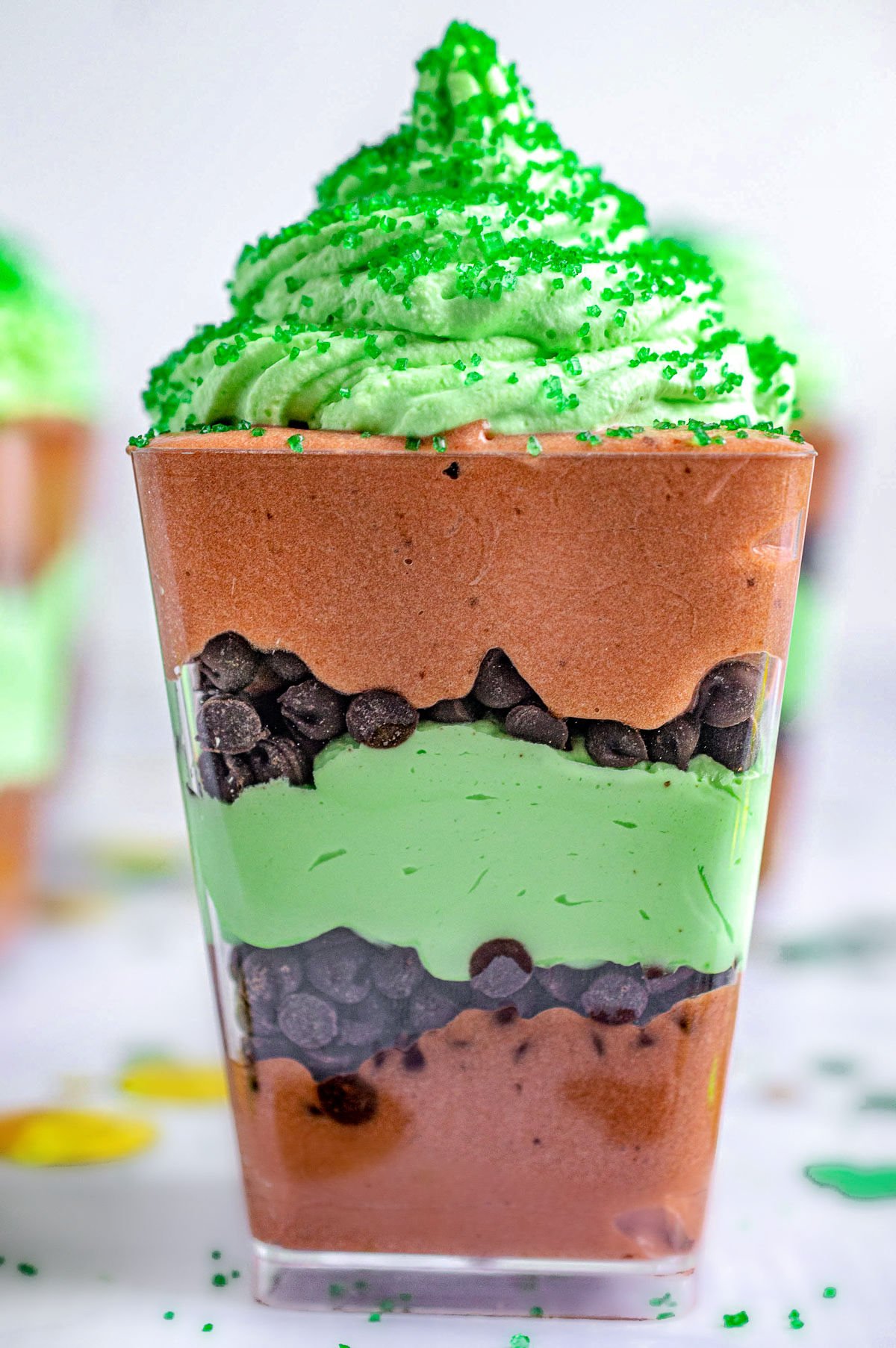 layered dessert with chocolate pudding and mint whipped cream in a clear plastic cup.