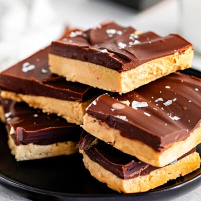 peanut butter chocolate bars stacked on black plate and sprinkled with sea salt.