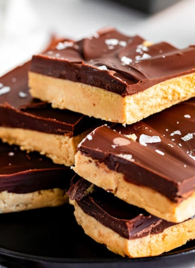 peanut butter chocolate bars stacked on black plate and sprinkled with sea salt.