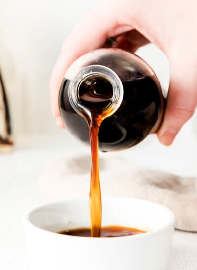 vanilla extract being poured from a bottle into a small white bowl.