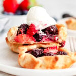 three mini berry galettes on small white plate topped with whipped cream.