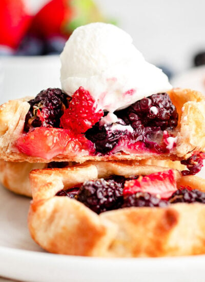 three mini berry galettes on small white plate topped with whipped cream.