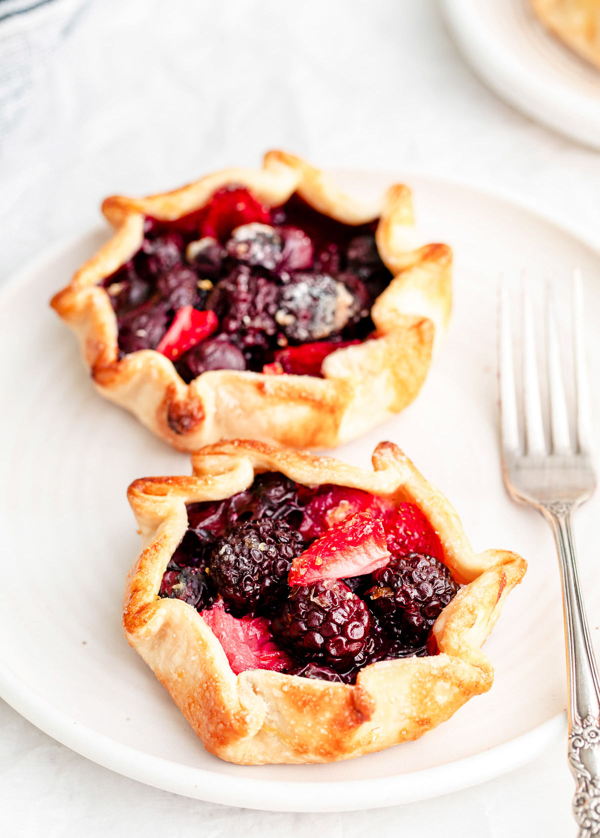 two mini galettes on a white plate with a fork