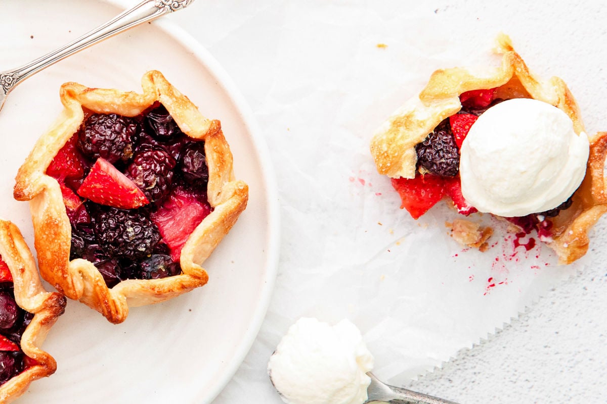 galette topped with ice cream and another berry galette sitting on white plate next to it.