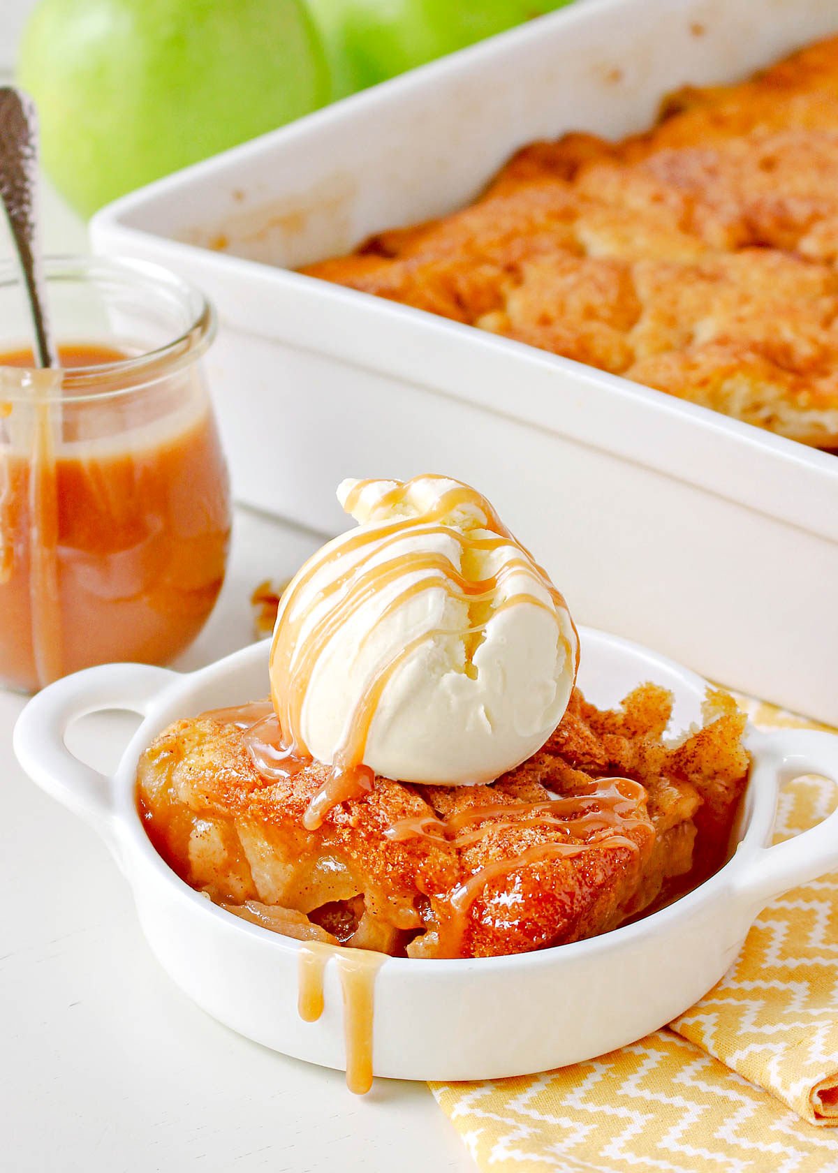 apple cobbler made with caramel sauce in small white dish topped with ice cream and salted caramel.