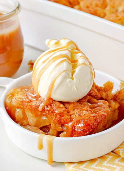 apple cobbler made with caramel sauce in small white dish topped with ice cream and salted caramel.