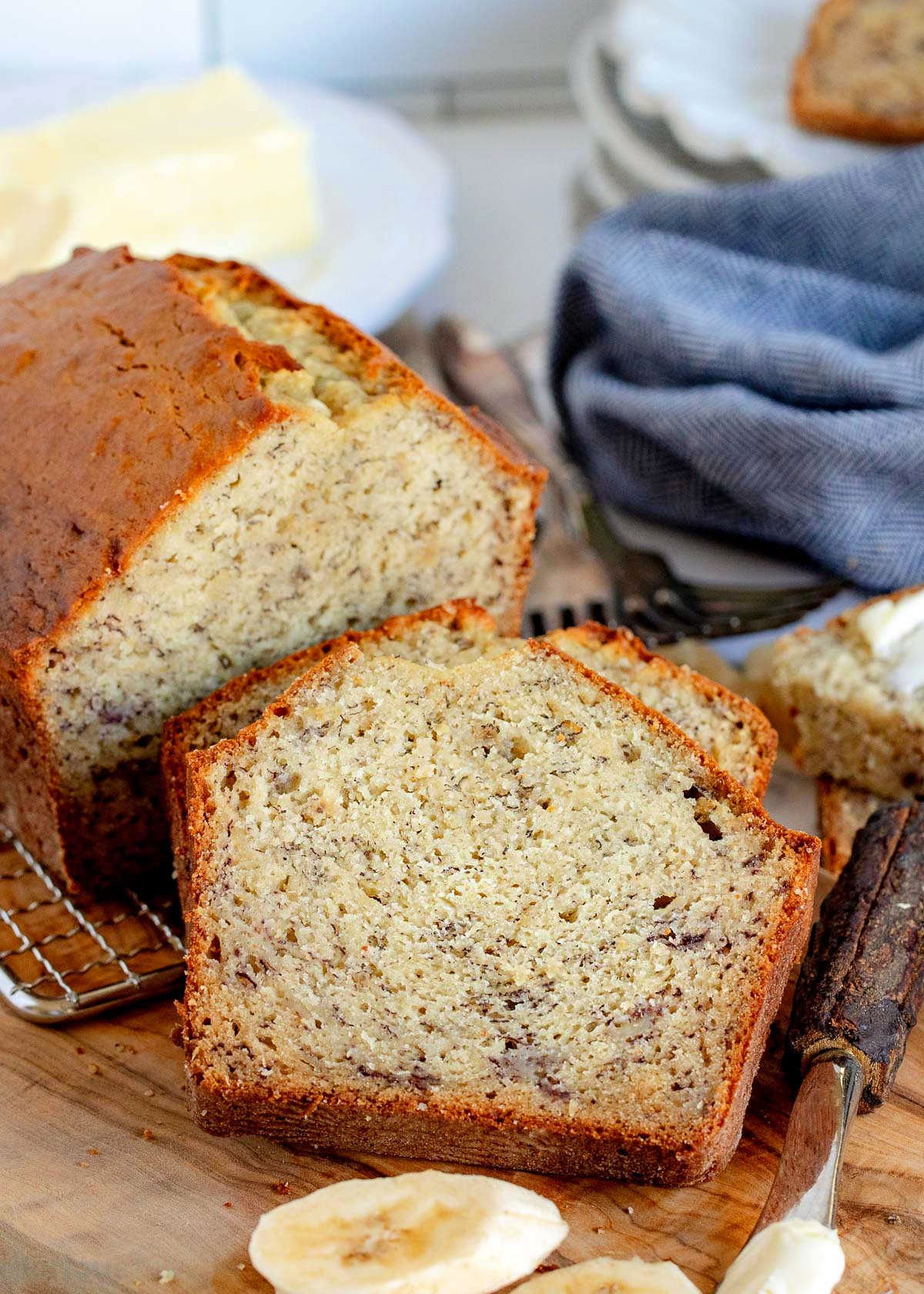 two slices of easy banana bread sitting on wood cutting board with the rest of the loaf in background with a stack of plates.