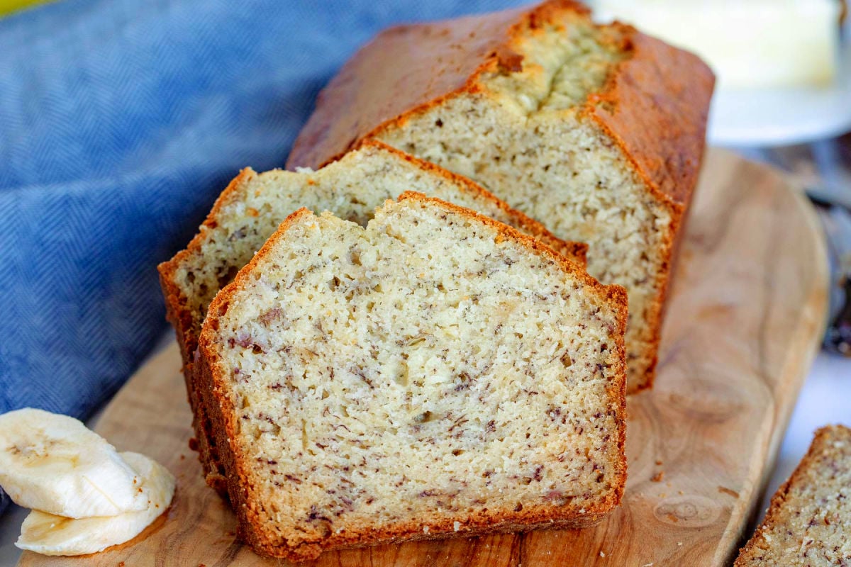 two slices of banana bread resting against the rest of the loaf in front of a blue napkin and sitting on a wood board.