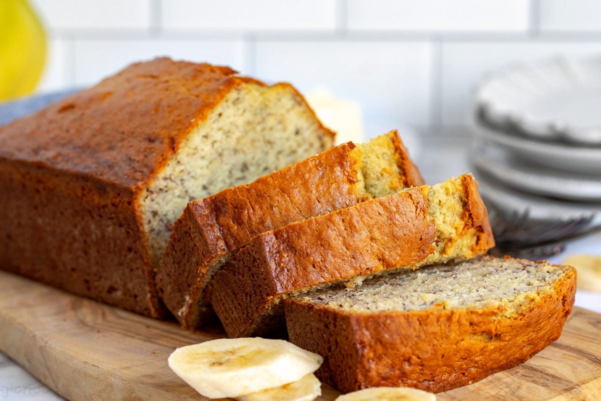 loaf of banana bread with three slices cut off and sitting on wood cutting board.