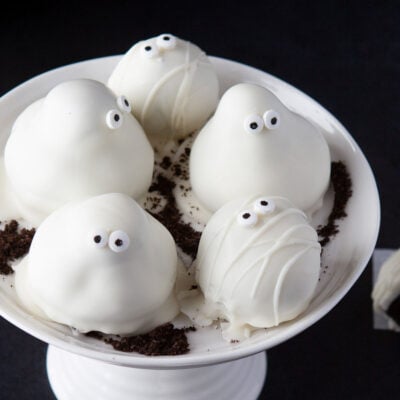 five Oreo truffles sitting on small white cake stand. decorated as ghosts and mummies for halloween.