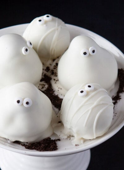 five Oreo truffles sitting on small white cake stand. decorated as ghosts and mummies for halloween.