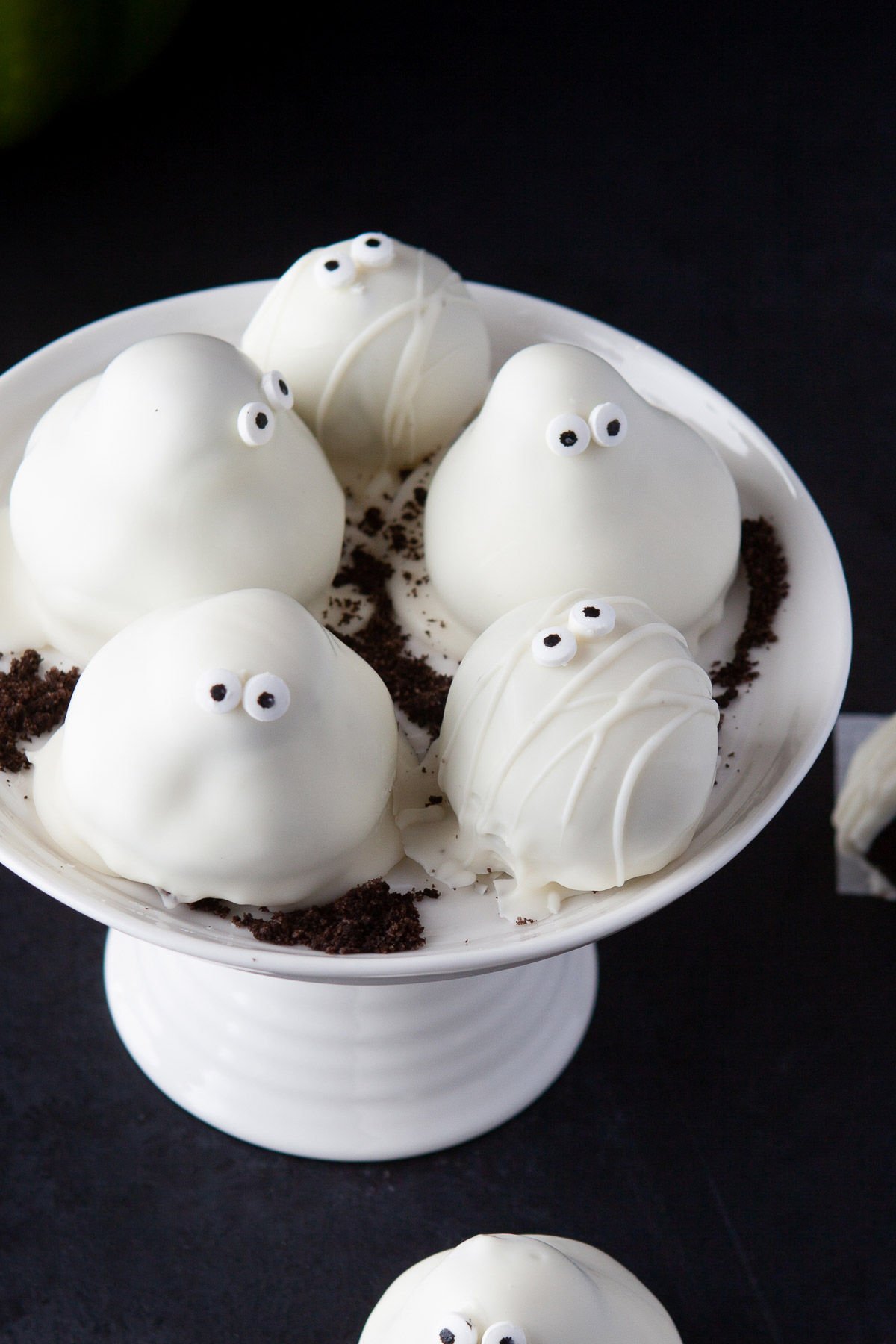 five Oreo truffles sitting on small white cake stand. decorated as ghosts and mummies for halloween.