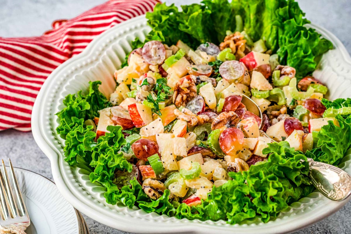 wide look at waldorf salad in a white bowl lined with lettuce leaves.