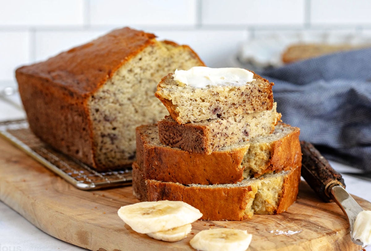 slice of banana bread cut in half and buttered sitting on two more slices bread. the banana bread is in the background.