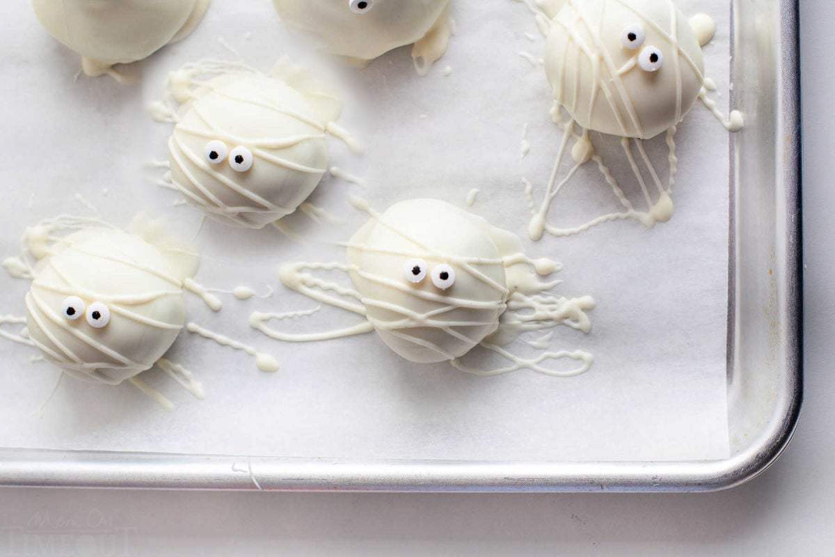 six mummy oreo balls on quarter sheet sitting on white parchment paper.