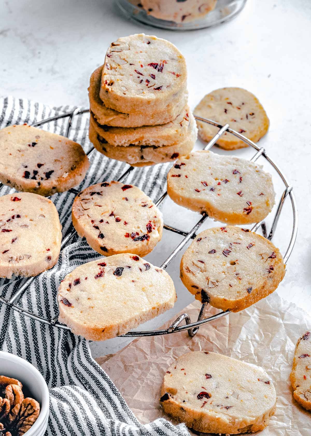 stacks of shortbread cookies are scattered on a round wire rack with a black and white striped towel underneath.