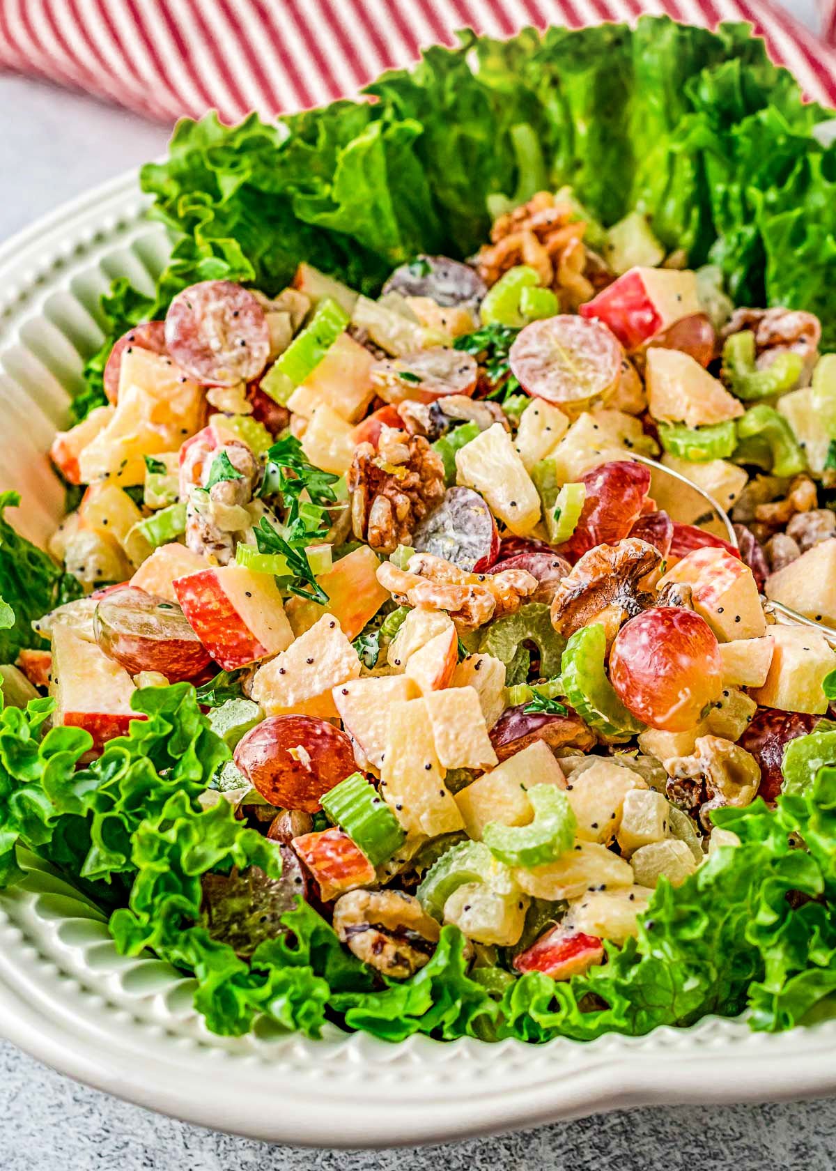 large white serving bowl filled with waldorf salad that is sitting on a bed of lettuce.