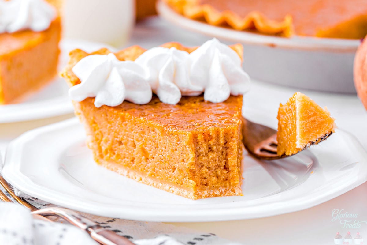 slice of sweet potato pie with a bite taken. the pie slice is topped with dollops of whipped cream and is sitting in front of the pie tin.