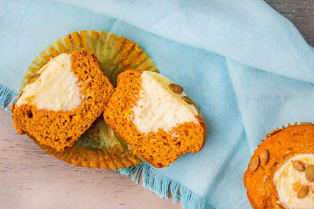 pumpkin cream cheese muffin cut in half and sitting in it's parchment muffin wrapper on a blue napkin.