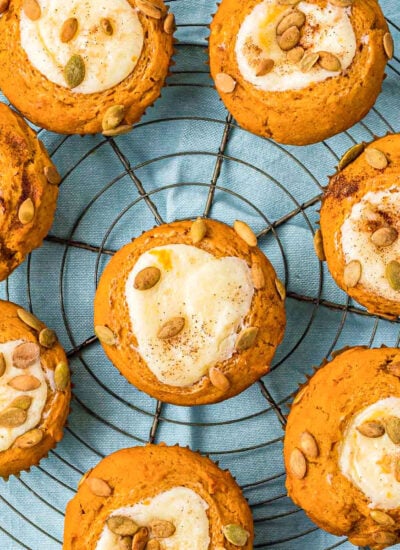 eight pumpkin muffins with cream cheese fillings are sitting on a wire rack on top of a light aqua colored napkin.