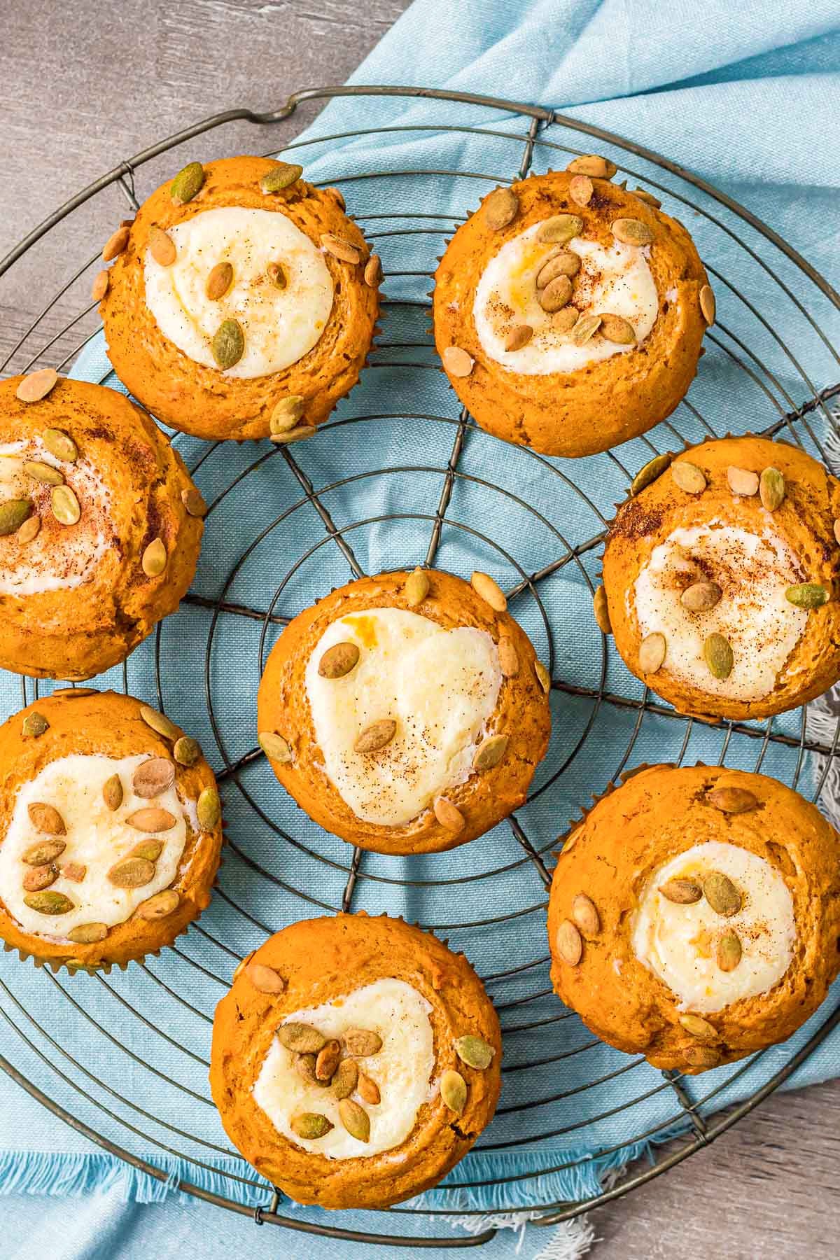 eight pumpkin muffins with cream cheese fillings are sitting on a wire rack on top of a light aqua colored napkin.