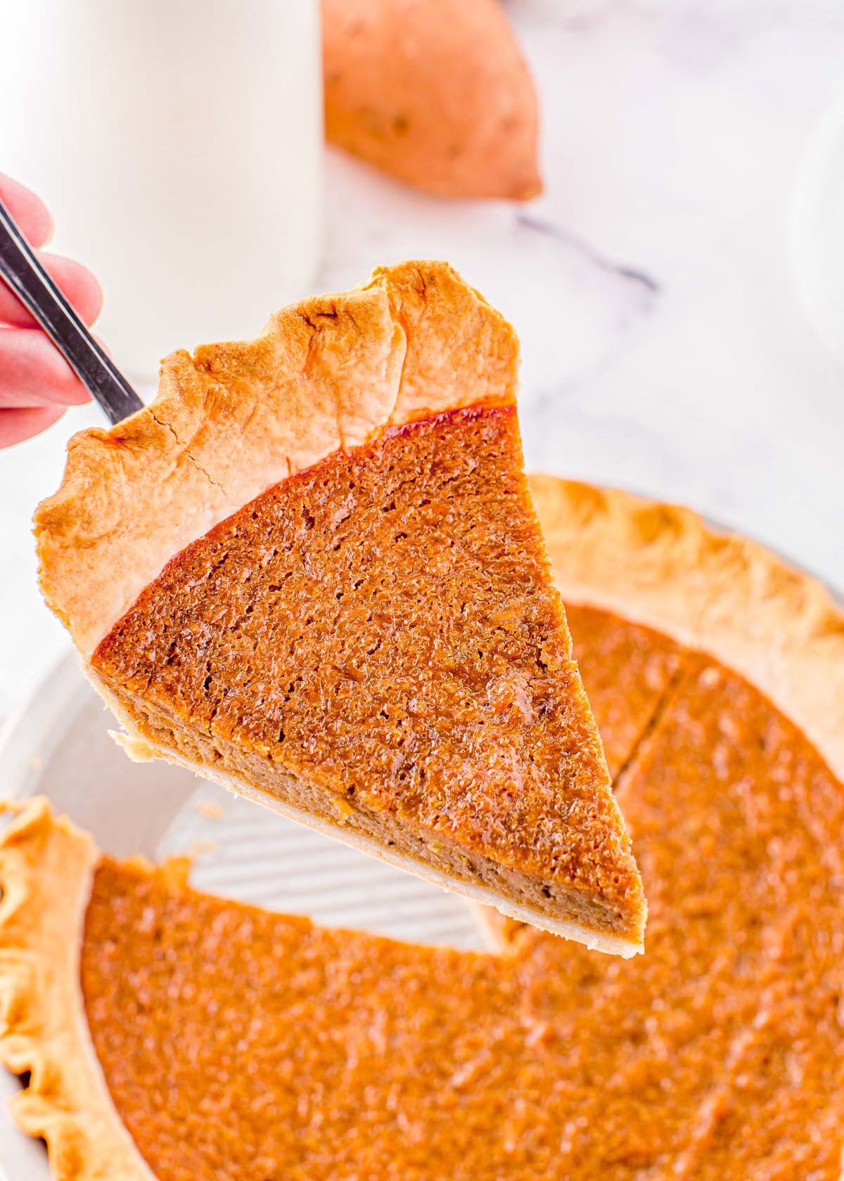 piece of sweet potato pie held up above pie with a pie server.