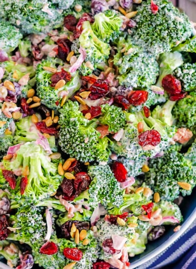 top down look at a broccoli salad made with bacon, cranberries and sunflower seeds in a blue bowl with a blue striped napkin next to it.