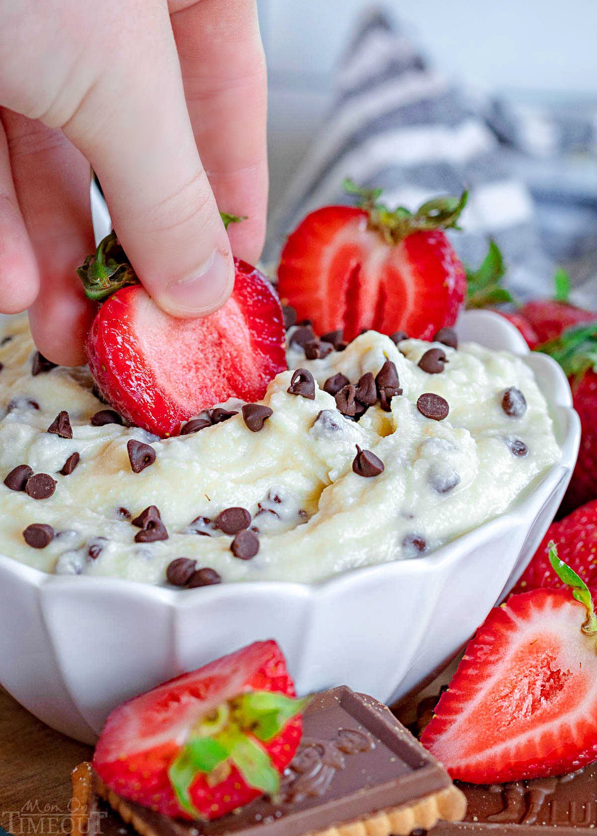 strawberry being dipped into cannoli dip in white bowl with more strawberries around the bowl.