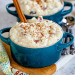 two small bowls filled with rice pudding and both have a cinnamon stick sticking out of the top. garnished with freshly grated cinnamon.