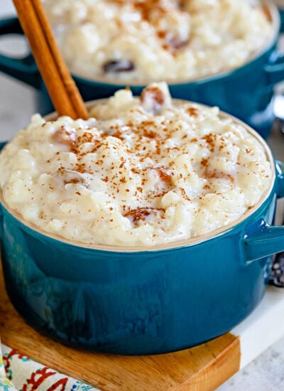 two small bowls filled with rice pudding and both have a cinnamon stick sticking out of the top. garnished with freshly grated cinnamon.