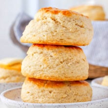 three buttermilk biscuits stacked on top of each other on a small white plate.