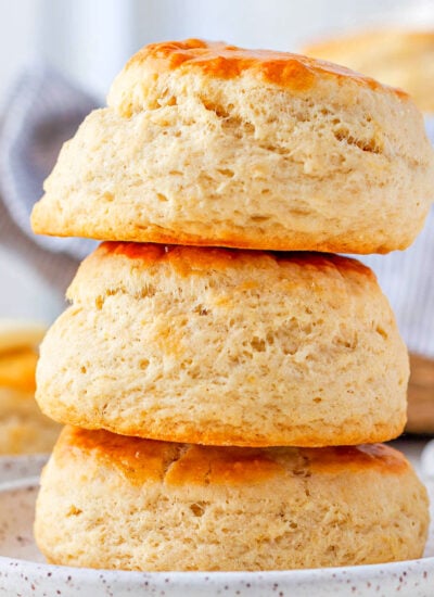 three buttermilk biscuits stacked on top of each other on a small white plate.