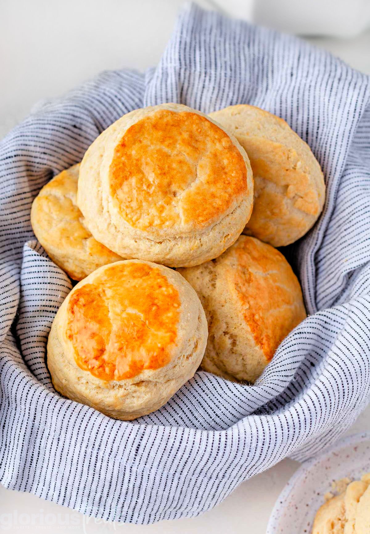 top down look at five biscuits in a basket that is lined with a blue and white towel. biscuits are golden brown on top.
