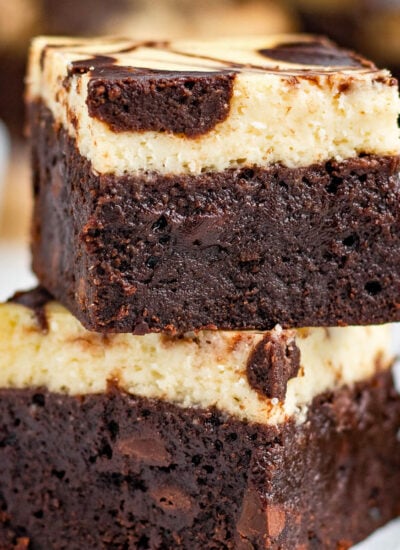 two brownies stacked on top of each other on a small white plate. more brownies can be seen in the background.