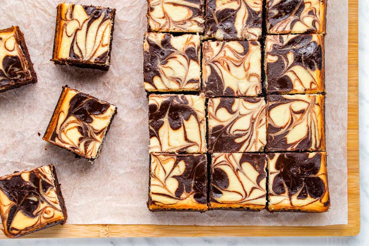 top down look at cheesecake brownies cut into small squares on a wood cutting board.