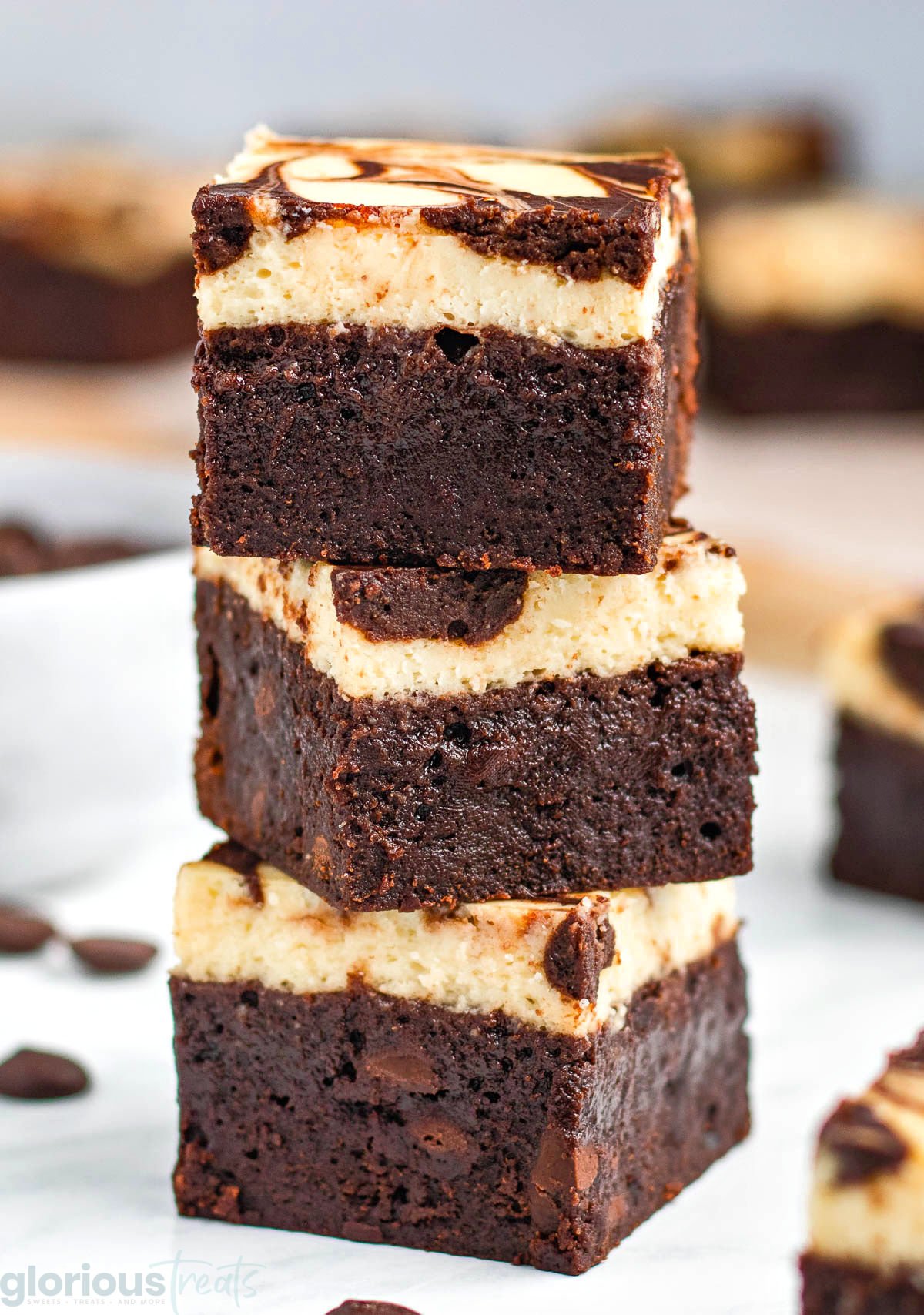 three cheesecake brownies stacked on top of each other with more brownies surround them.