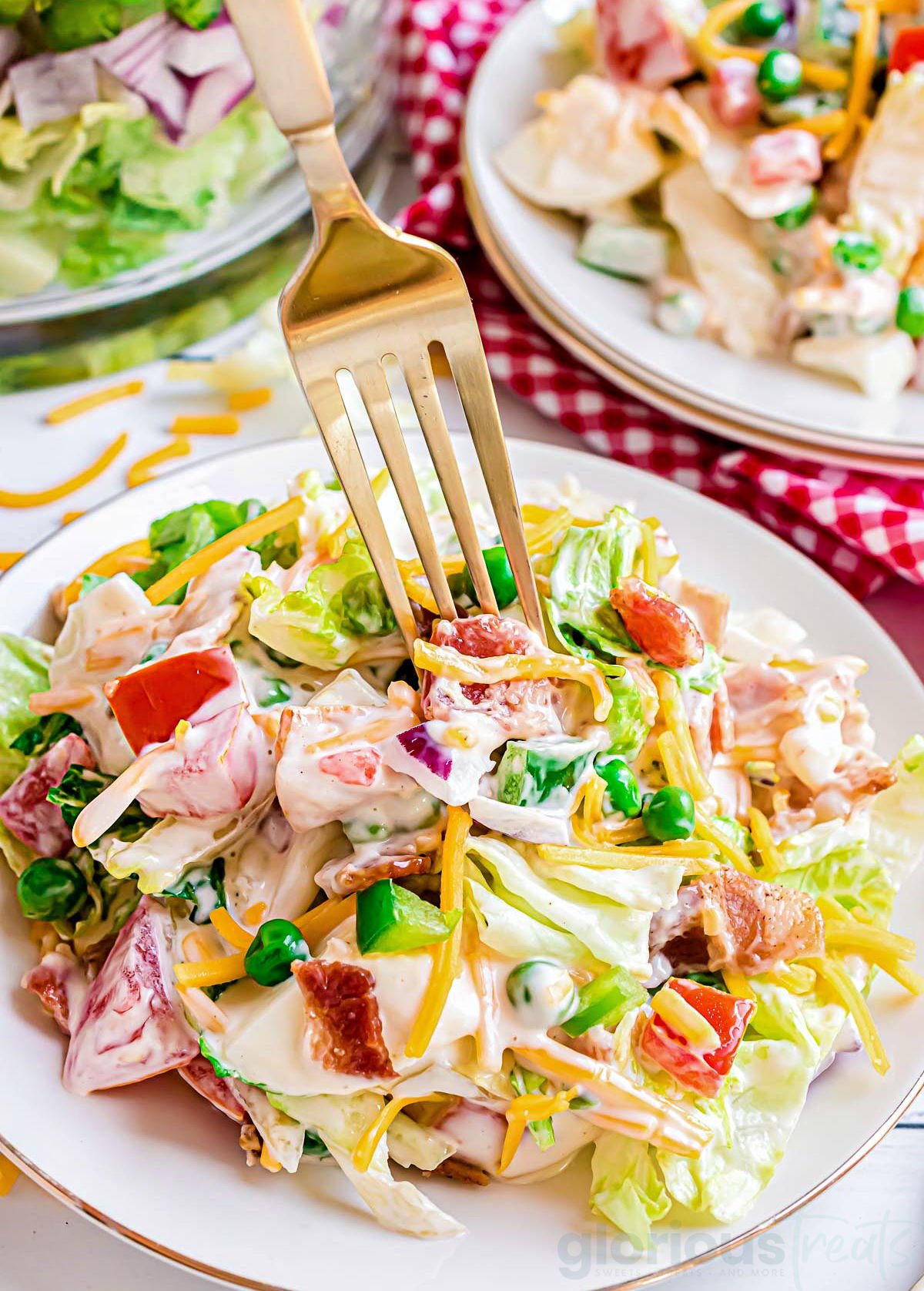 seven layer salad plated with dressing on top an da gold fork is taking a bite of the salad.