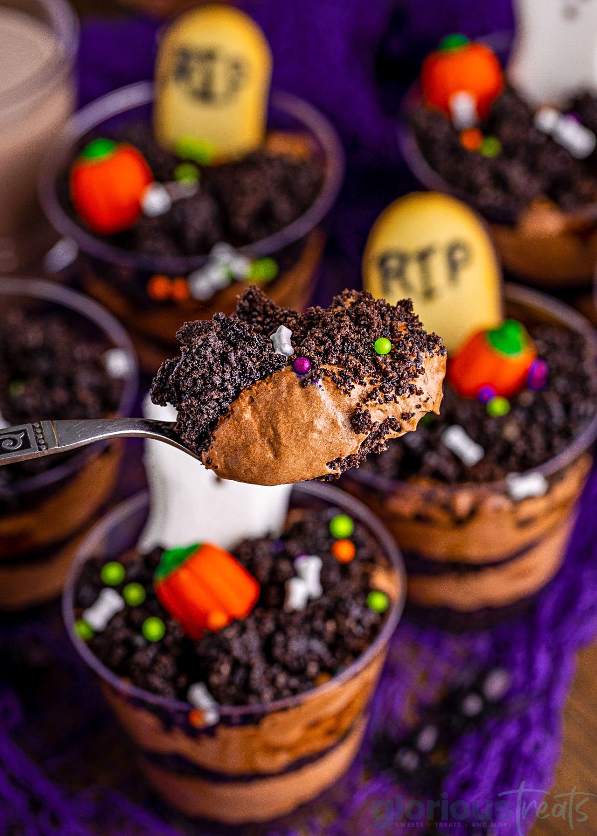 spoonful of pudding from the dirt cups held up over six or so assembled halloween pudding cups.