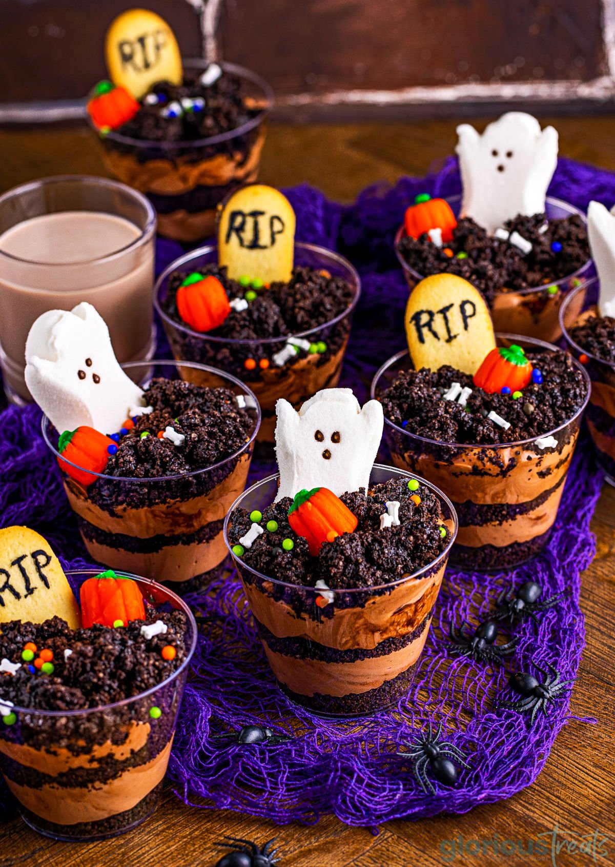 halloween pudding dirt cups displayed on a purple net and topped with ghost peeps and milano cookie tombstones.