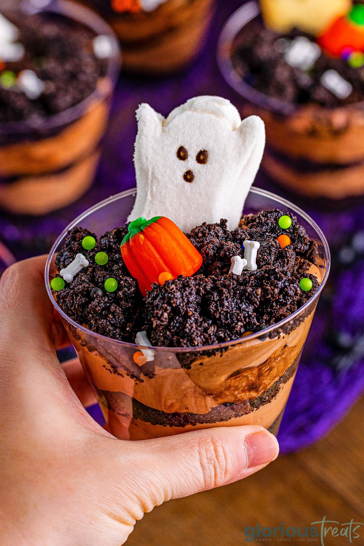hand holding a single pudding dirt cup topped with a pumpkin candy and ghost peeps.