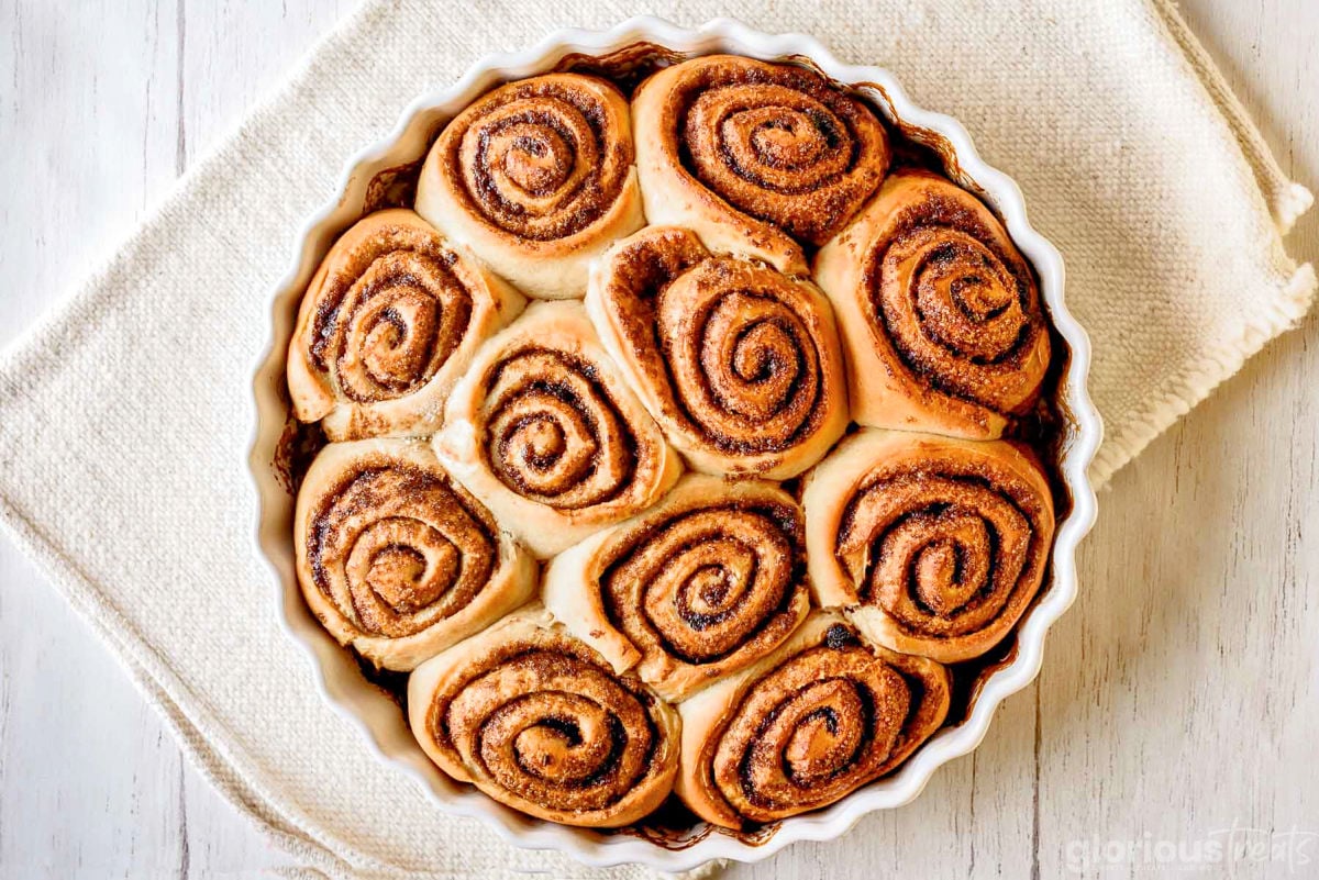 top down look at cinnamon rolls freshly baked in white, round baking dish sitting on white towel.