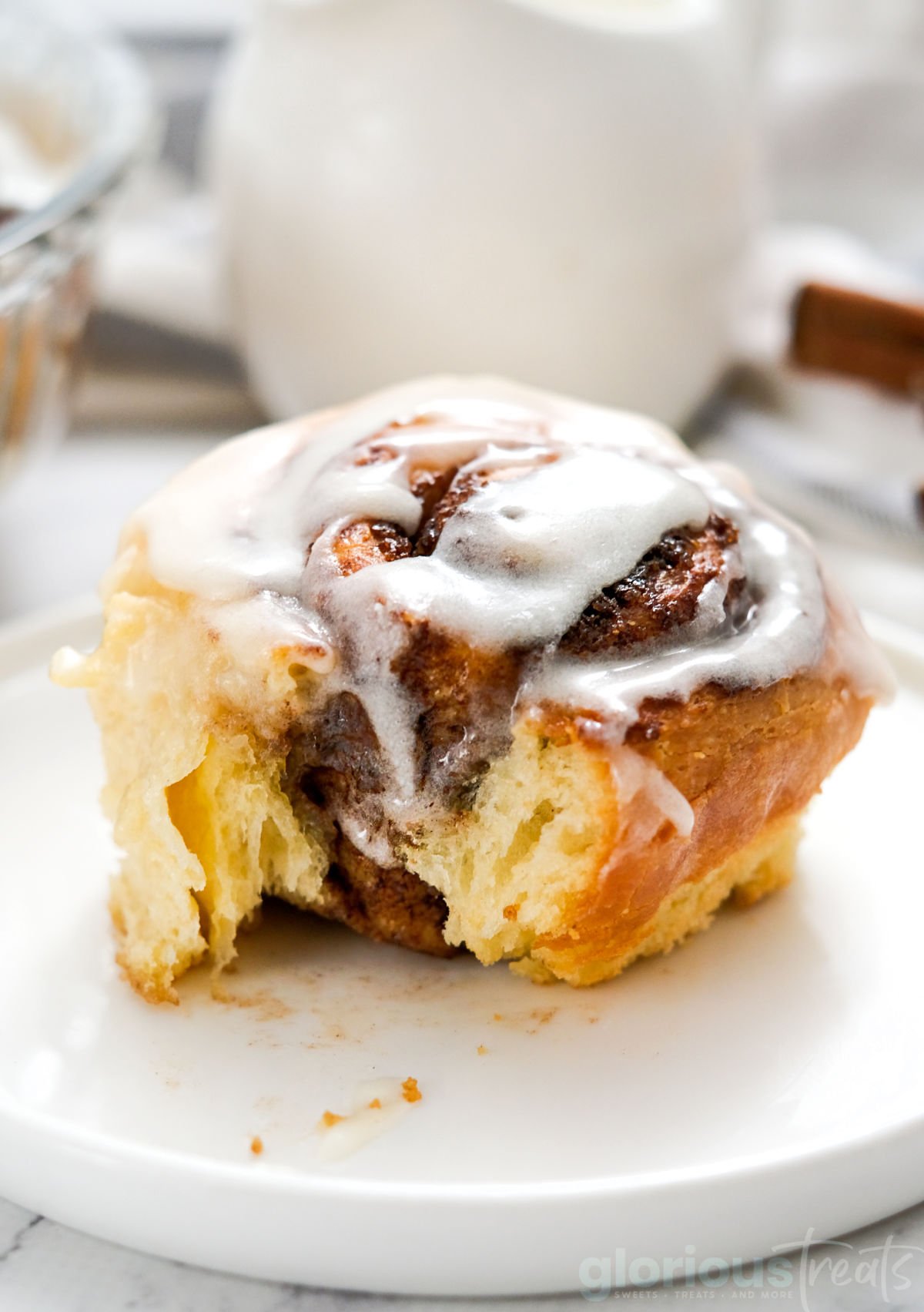 cinnamon roll with bite taken sitting on white round plate. topped with cream cheese icing.