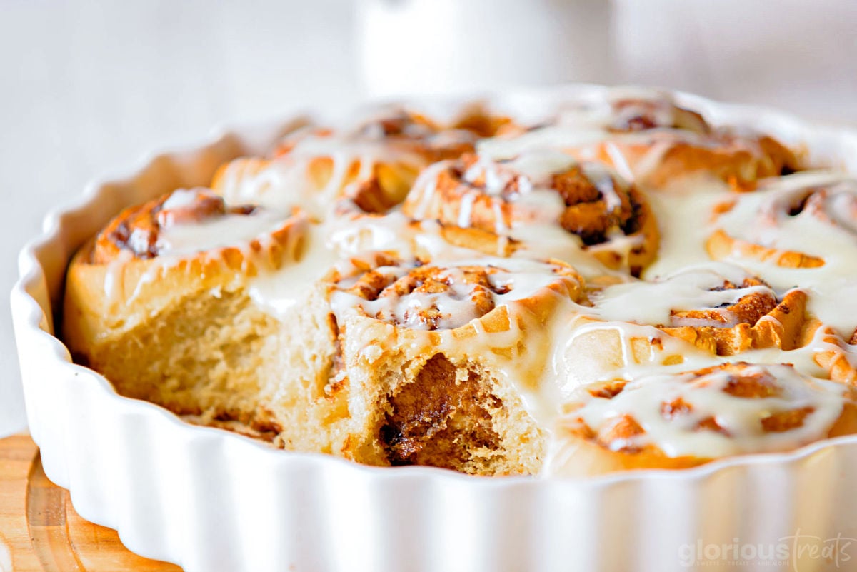 shot of a round white casserole dish with cinnamon rolls in it. two rolls have been removed.